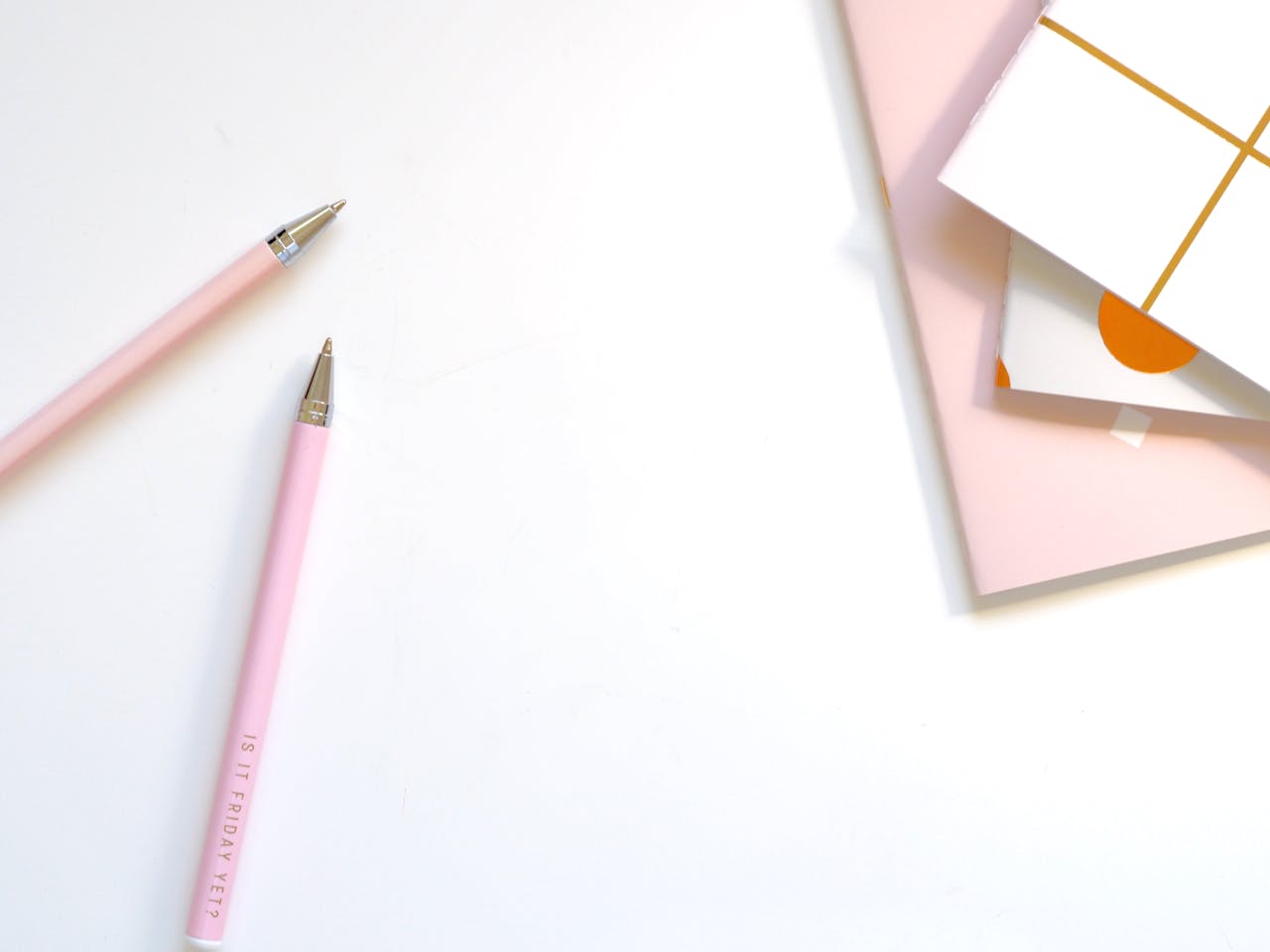 A minimalist flat lay of pink pens and pastel notebooks on a smooth white background, ideal for office and school themes.